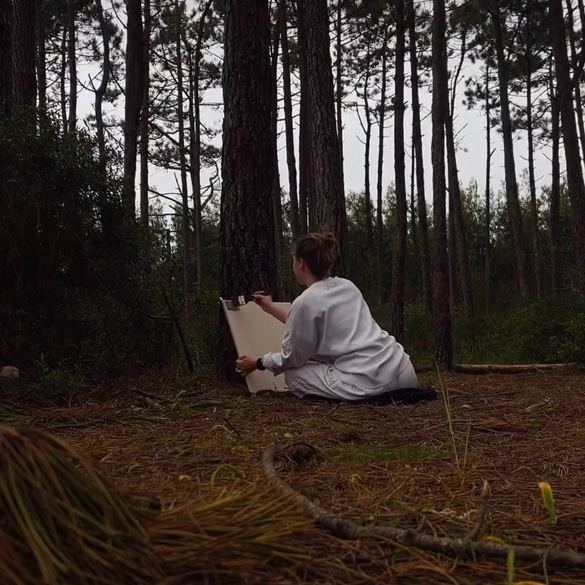 The artist sitting on the forest floor, painting among the pines